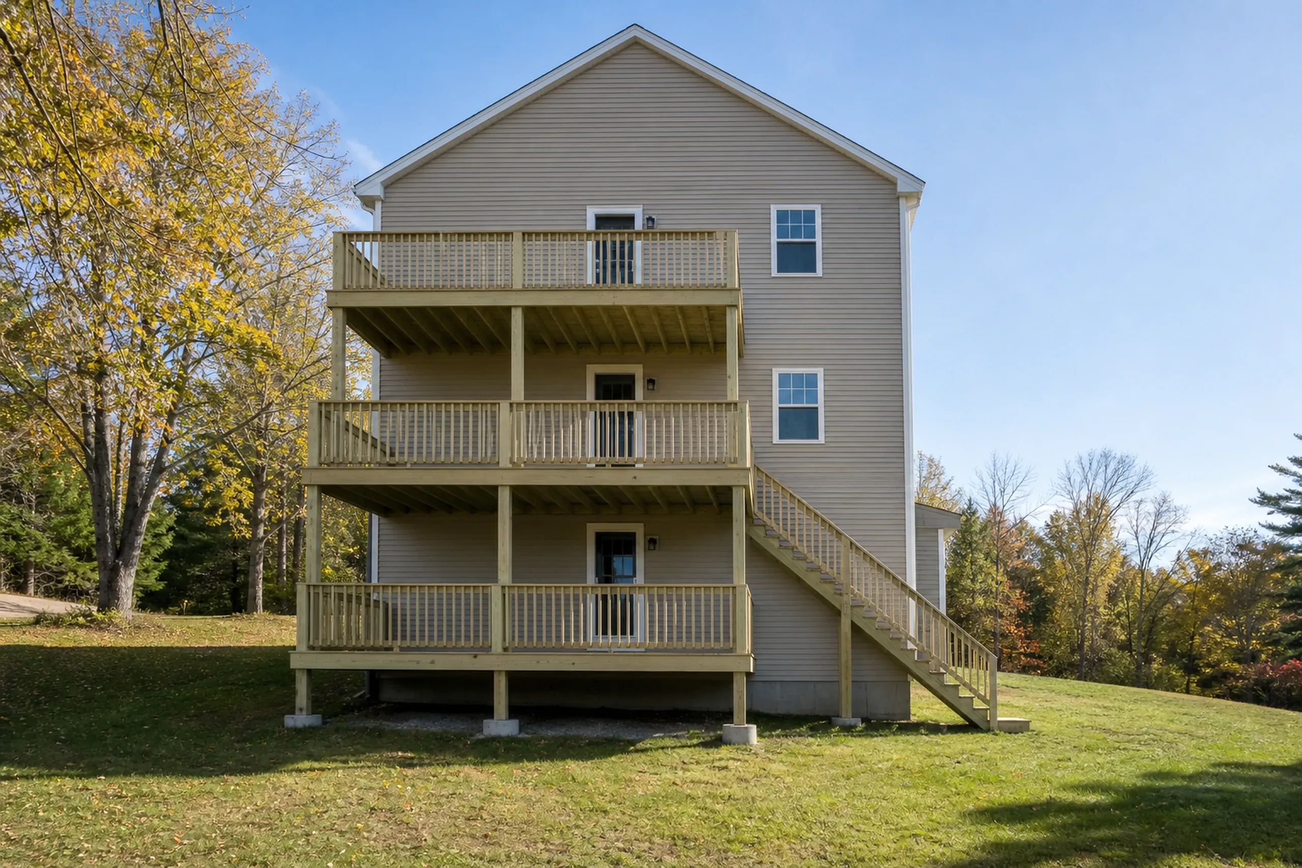 Three-level wooden deck with railings on the back of a beige two-story house, with stairs on the right and two people on the second deck.
